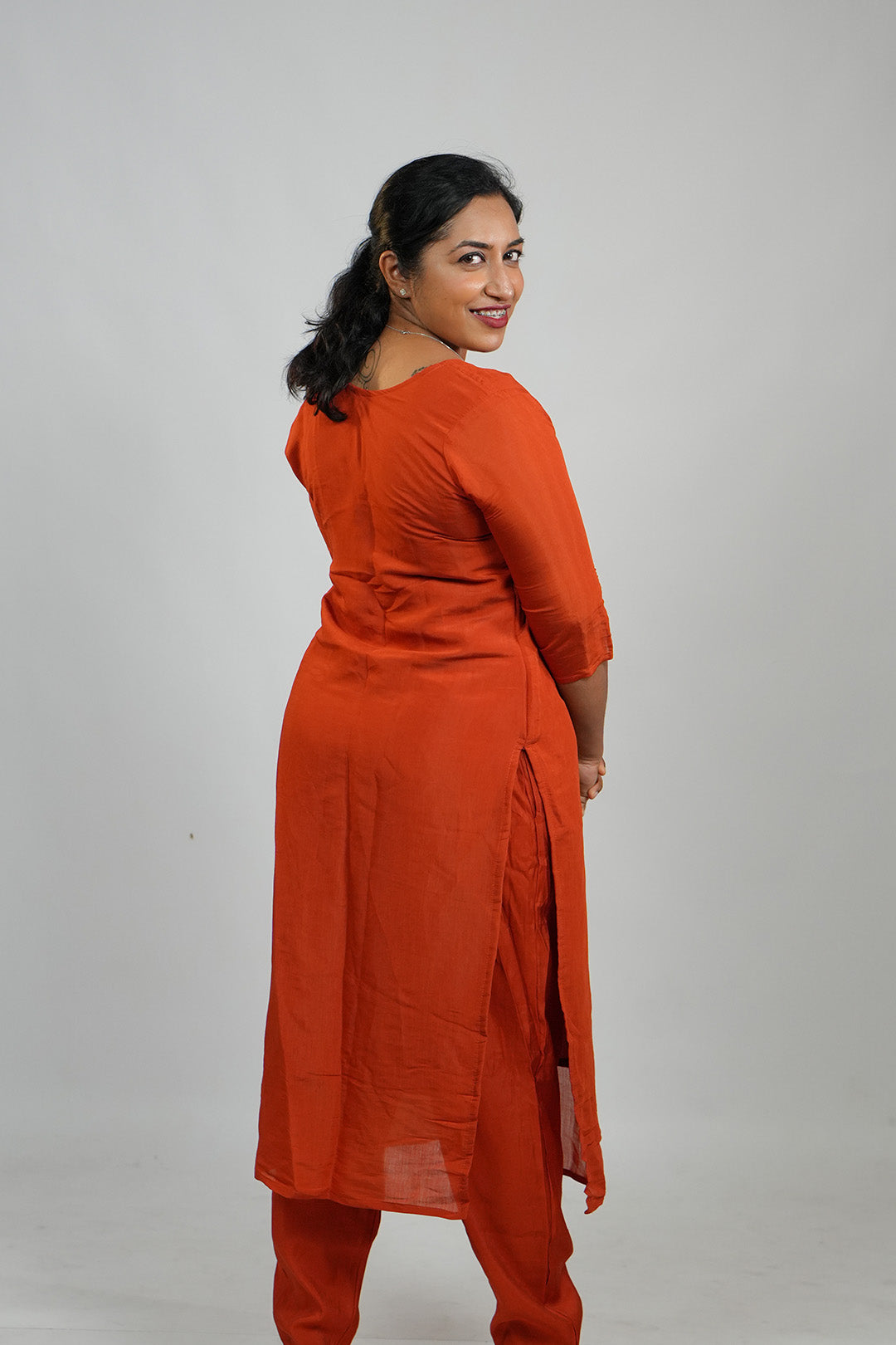 Woman in Aroha Ember Leaf terracotta co-ord set posing with an over the shoulder look
